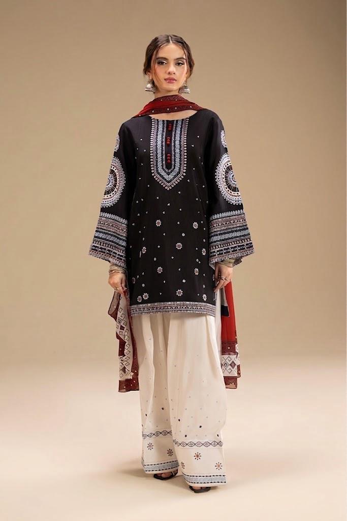 A woman modeling a traditional South Asian outfit featuring a black kurta with intricate white and blue embroidery, paired with wide-leg cream trousers and a red dupatta, set against a solid beige studio background.