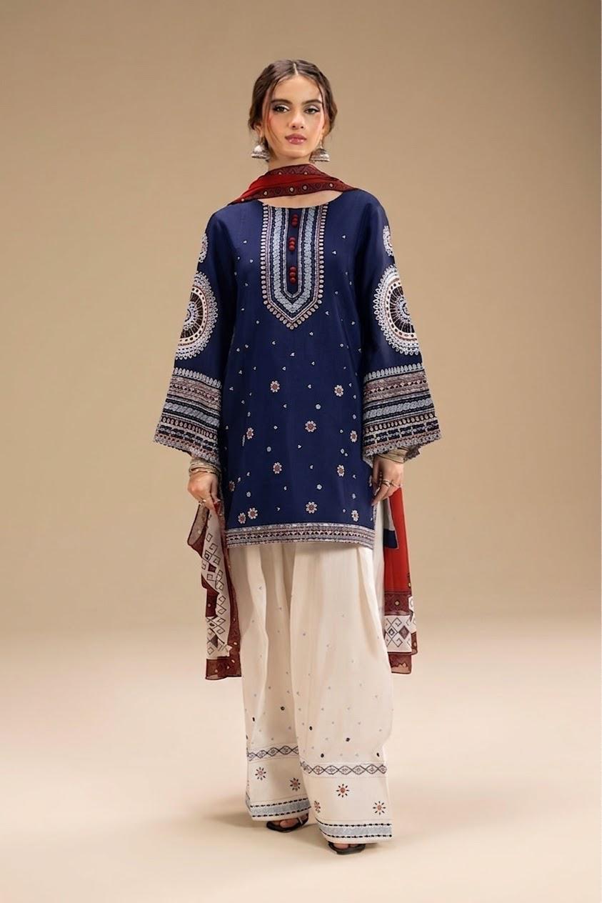 A woman modeling a traditional South Asian outfit consisting of a navy blue kurta with intricate white and red embroidery, paired with white wide-leg trousers and a red dupatta, set against a solid beige studio background.